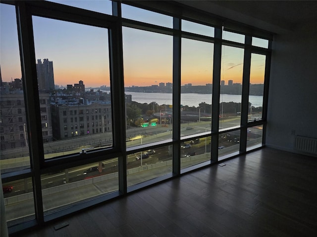 unfurnished room featuring radiator heating unit, dark wood-type flooring, floor to ceiling windows, and a water view