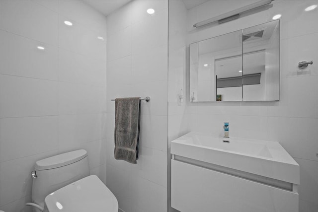 bathroom with vanity, toilet, and tile walls