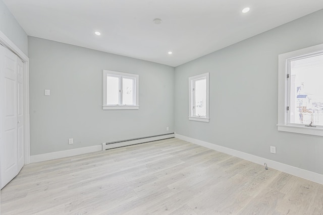 unfurnished room with a baseboard heating unit and light wood-type flooring