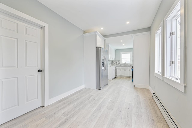 interior space featuring white cabinetry, appliances with stainless steel finishes, a baseboard heating unit, and light hardwood / wood-style floors