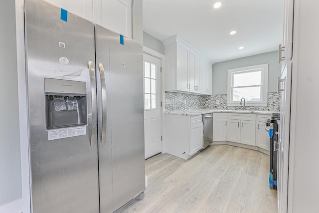 kitchen featuring tasteful backsplash, white cabinetry, sink, stainless steel appliances, and light wood-type flooring