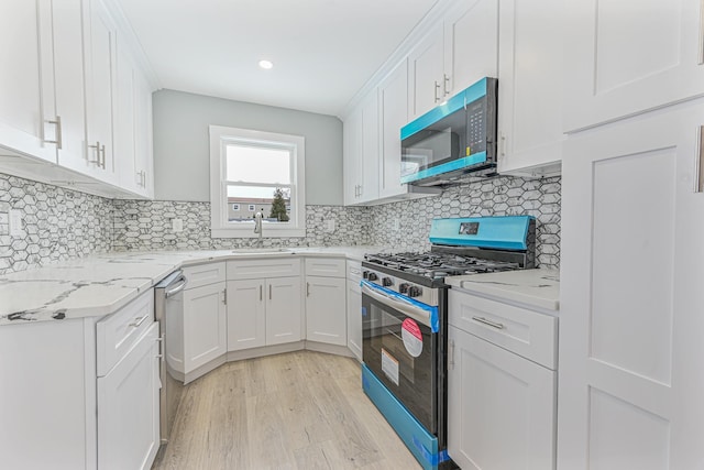 kitchen featuring appliances with stainless steel finishes, sink, white cabinets, decorative backsplash, and light stone counters