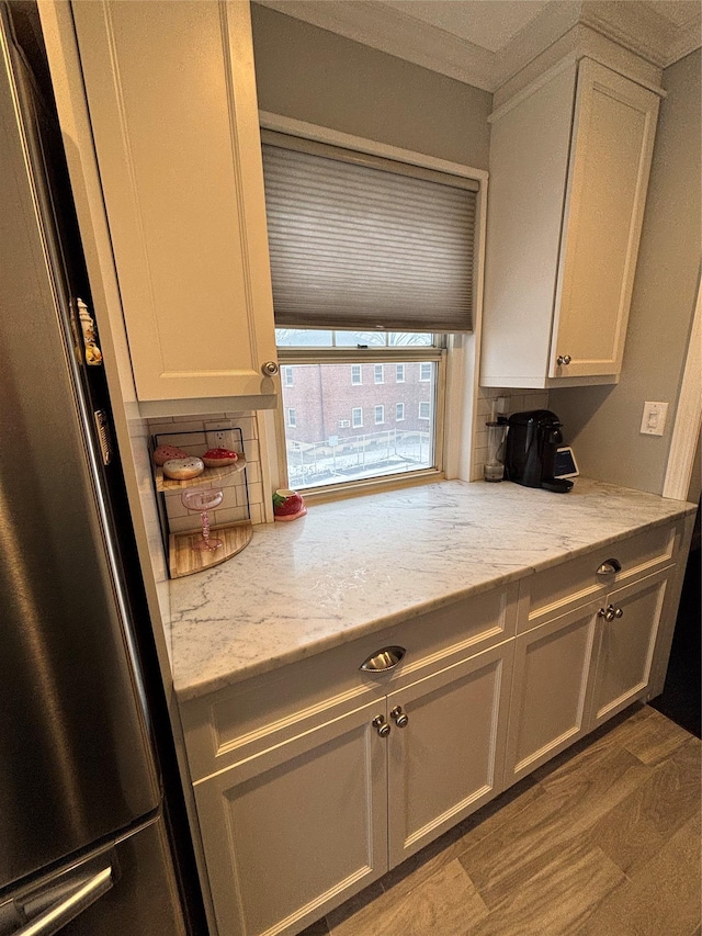 kitchen featuring stainless steel fridge, white cabinetry, light stone counters, light hardwood / wood-style floors, and decorative backsplash