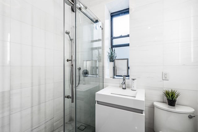 bathroom featuring vanity, toilet, a shower with door, and tile walls