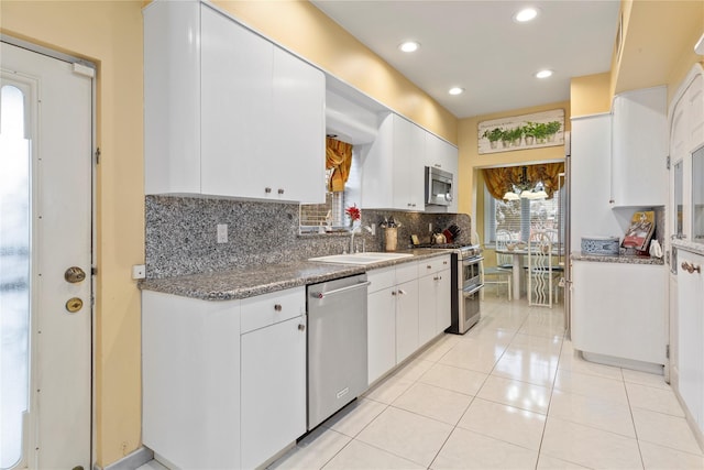 kitchen featuring tasteful backsplash, white cabinets, dark stone counters, appliances with stainless steel finishes, and a sink