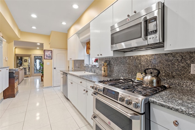 kitchen with stainless steel appliances, dark stone countertops, a sink, and white cabinetry