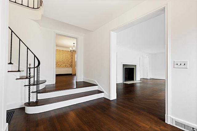 interior space with parquet floors, a notable chandelier, visible vents, a fireplace with flush hearth, and baseboards