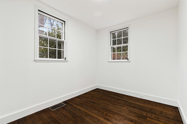 spare room with dark wood-style flooring, visible vents, and baseboards