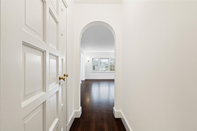 hall featuring baseboards, arched walkways, and dark wood-style flooring