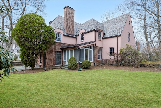 rear view of house featuring brick siding, a lawn, a chimney, and stucco siding