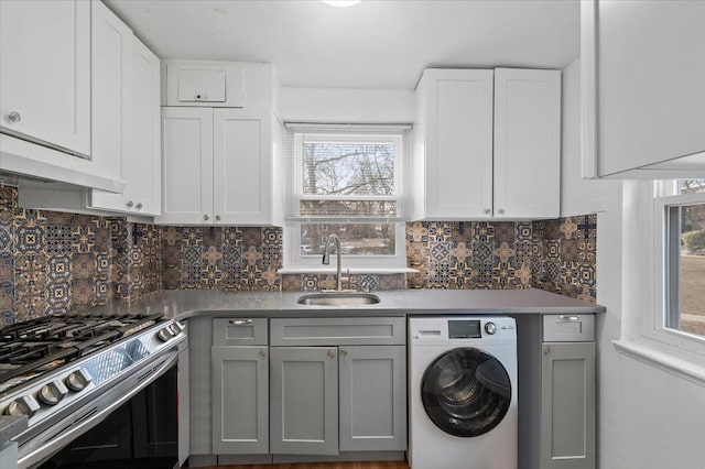 kitchen featuring gray cabinetry, white cabinets, stainless steel range with gas stovetop, a sink, and washer / dryer