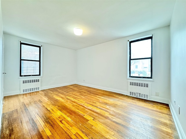 unfurnished room featuring radiator heating unit and light hardwood / wood-style floors