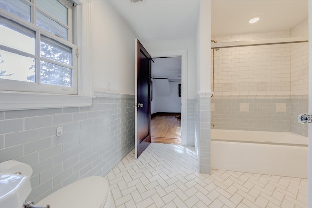 bathroom with tile patterned flooring, tiled shower / bath combo, tile walls, and toilet