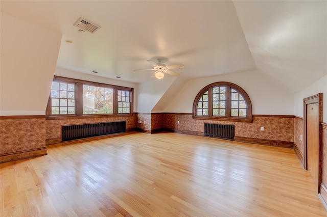 unfurnished living room featuring radiator heating unit, a healthy amount of sunlight, and light wood-type flooring