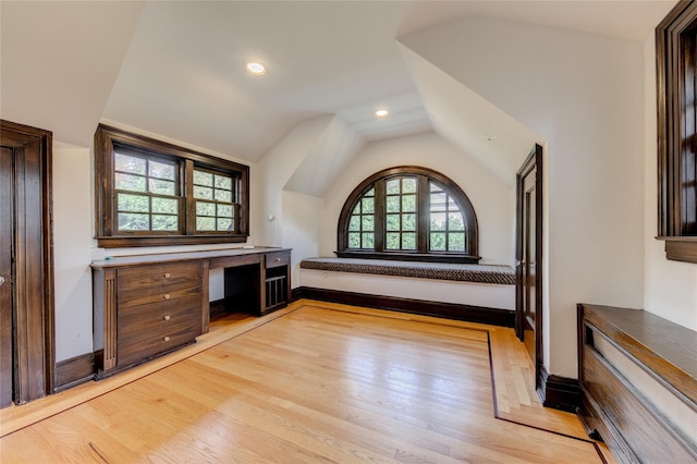 unfurnished office with lofted ceiling, built in desk, and light hardwood / wood-style flooring