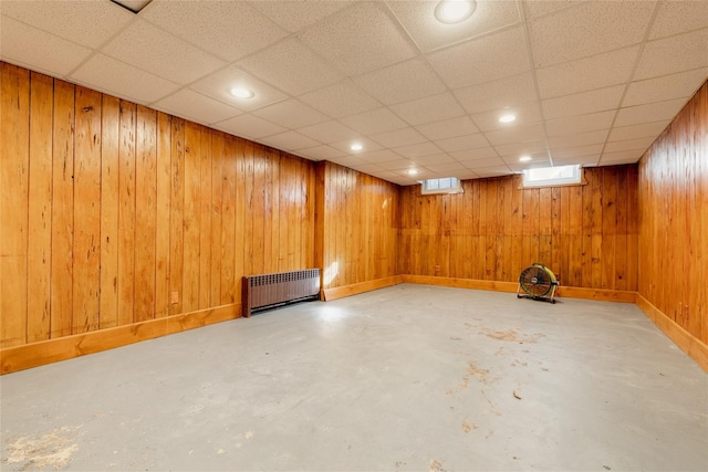 basement featuring radiator heating unit, a drop ceiling, and wood walls