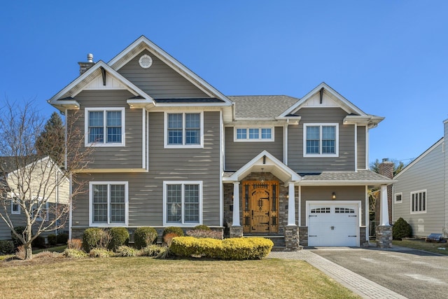 craftsman-style home featuring aphalt driveway, a front yard, a shingled roof, and a garage