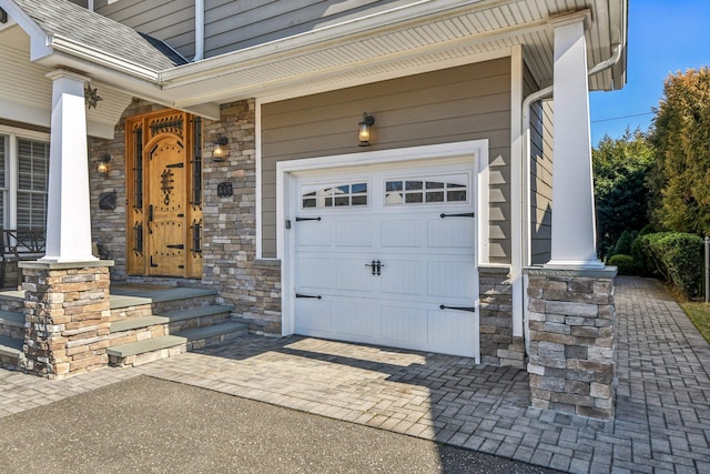 property entrance with decorative driveway, stone siding, and a garage