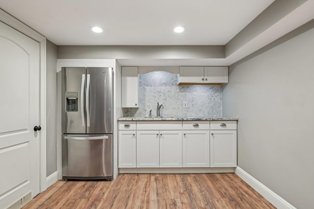 kitchen with stainless steel fridge, tasteful backsplash, baseboards, light wood-style floors, and a sink