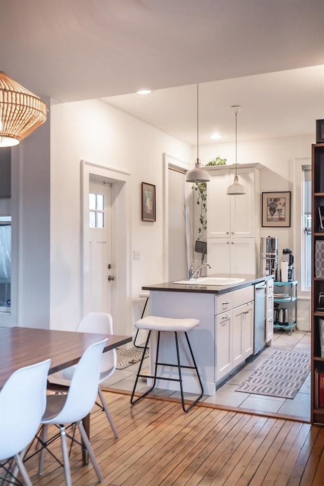 kitchen with sink, white cabinetry, hanging light fixtures, light wood-type flooring, and a kitchen island with sink