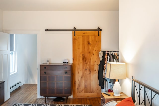 bedroom with a baseboard radiator, a barn door, and wood-type flooring