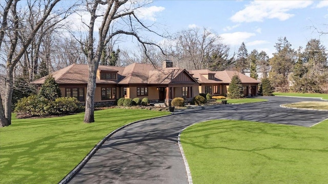 view of front of house featuring a chimney, aphalt driveway, board and batten siding, and a front yard