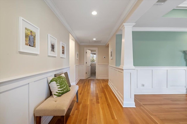 hallway with light wood-type flooring, crown molding, and ornate columns