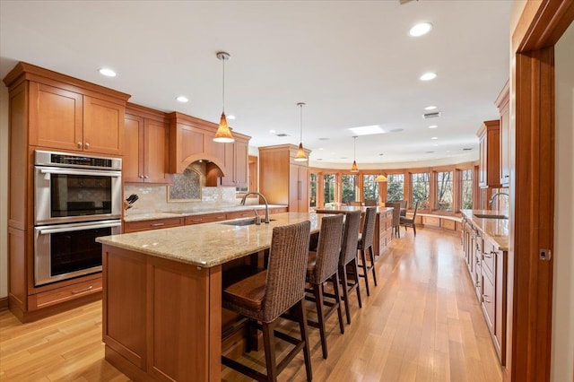 kitchen with double oven, sink, pendant lighting, and a center island with sink