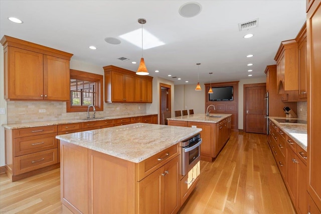 kitchen with an island with sink, hanging light fixtures, light hardwood / wood-style floors, sink, and black electric stovetop