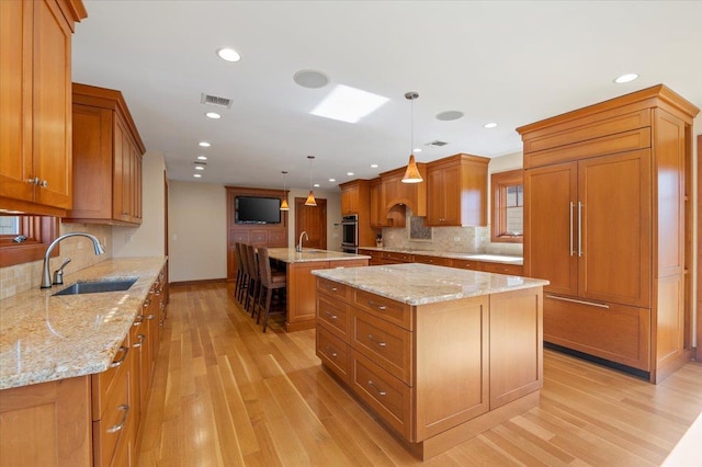 kitchen featuring sink, pendant lighting, light stone countertops, and a center island