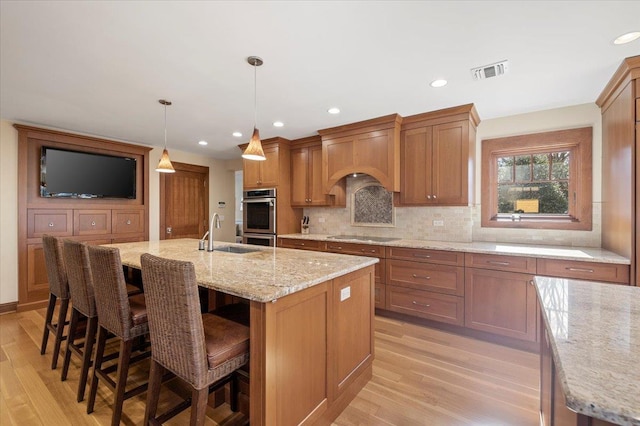 kitchen with an island with sink, sink, a breakfast bar area, double oven, and pendant lighting