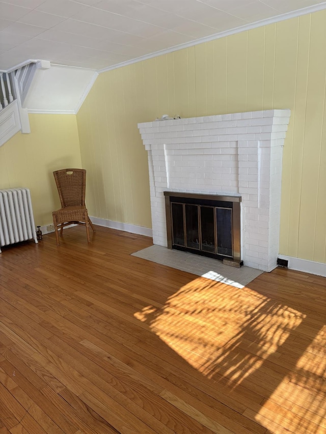 unfurnished room with hardwood / wood-style floors, radiator heating unit, a fireplace, lofted ceiling, and crown molding