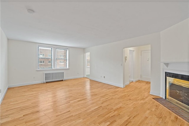 unfurnished living room featuring a tiled fireplace, radiator heating unit, and light hardwood / wood-style floors