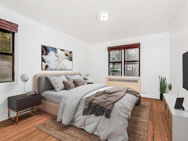 bedroom with radiator heating unit, wood finished floors, and baseboards