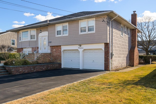 split foyer home with driveway, brick siding, a chimney, an attached garage, and a front yard