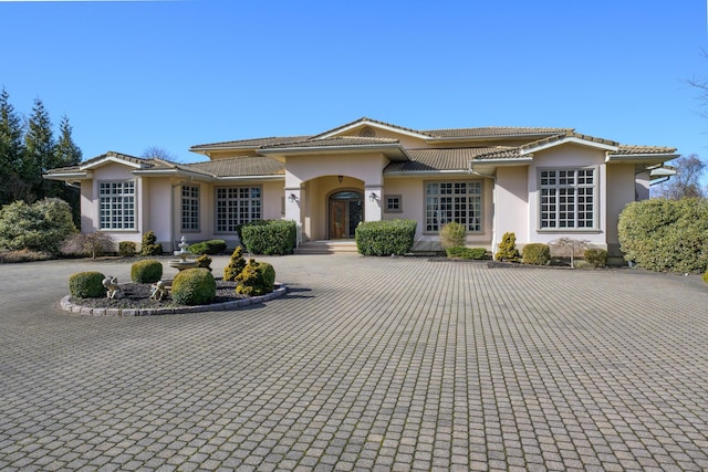 view of front of property featuring a tiled roof, decorative driveway, and stucco siding