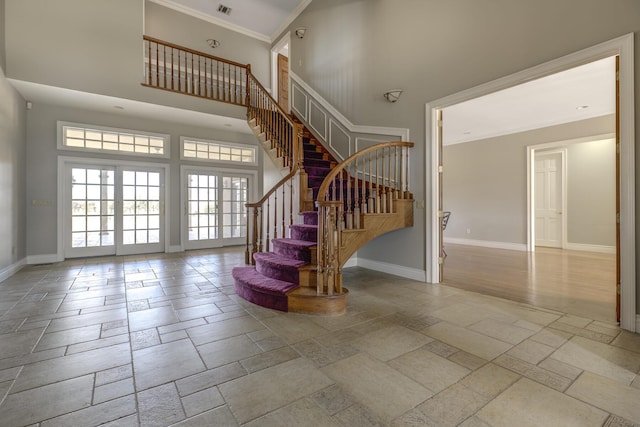 stairway with crown molding, stone tile flooring, visible vents, a towering ceiling, and baseboards