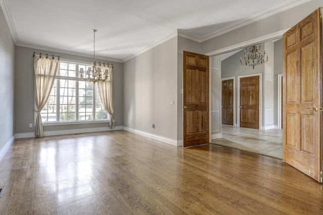 spare room featuring a chandelier, wood finished floors, visible vents, baseboards, and crown molding