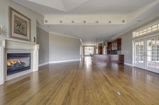 unfurnished living room with ornamental molding, a lit fireplace, french doors, and wood finished floors