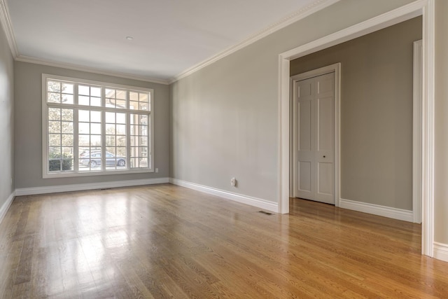 empty room with ornamental molding, wood finished floors, and baseboards