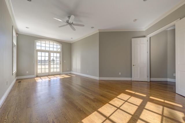 empty room with ornamental molding, wood finished floors, a ceiling fan, and baseboards