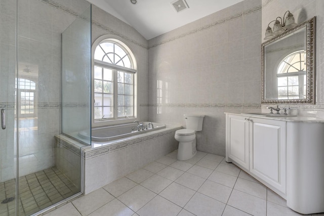 bathroom with lofted ceiling, tile patterned flooring, toilet, tile walls, and a stall shower