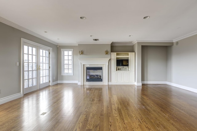 unfurnished living room featuring a glass covered fireplace, wood finished floors, visible vents, and baseboards