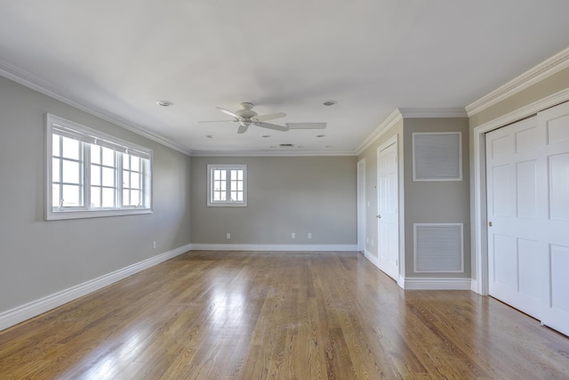 empty room with baseboards, visible vents, a ceiling fan, wood finished floors, and crown molding