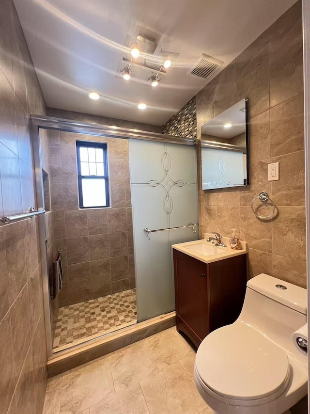 bathroom with a shower with door, vanity, tile walls, and toilet