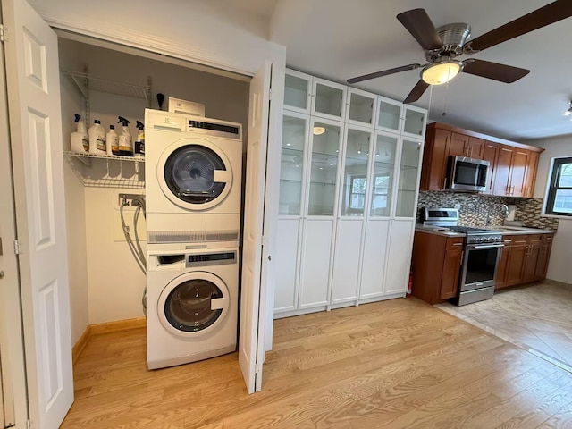 laundry room with ceiling fan, stacked washing maching and dryer, and light hardwood / wood-style flooring