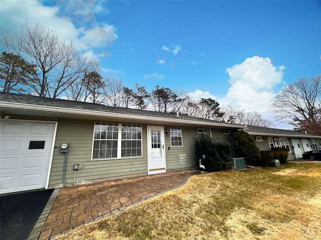 view of front of property with an attached garage, a front lawn, and central AC