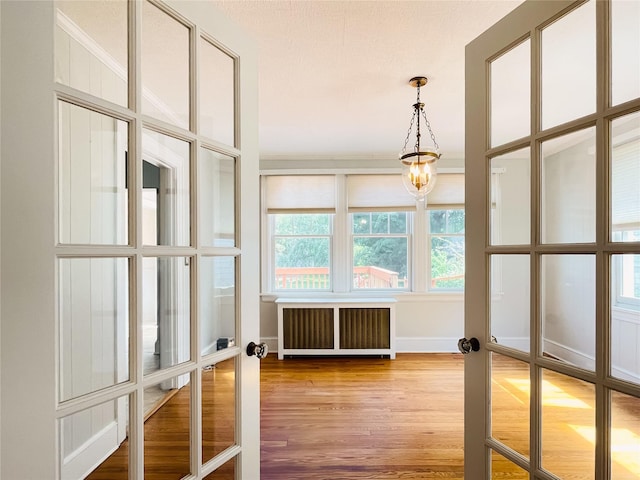 unfurnished sunroom featuring an inviting chandelier, radiator, and french doors