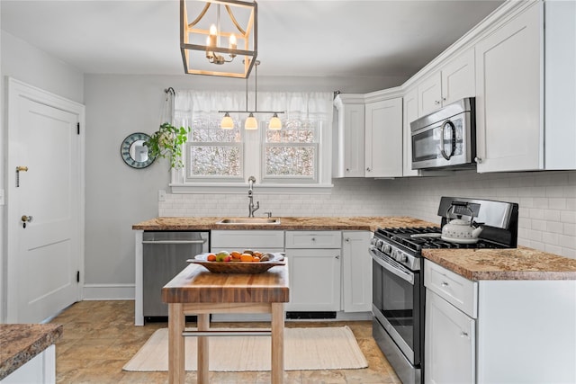 kitchen with appliances with stainless steel finishes, white cabinetry, sink, decorative backsplash, and hanging light fixtures