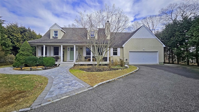 cape cod house with covered porch, a garage, driveway, roof with shingles, and a chimney